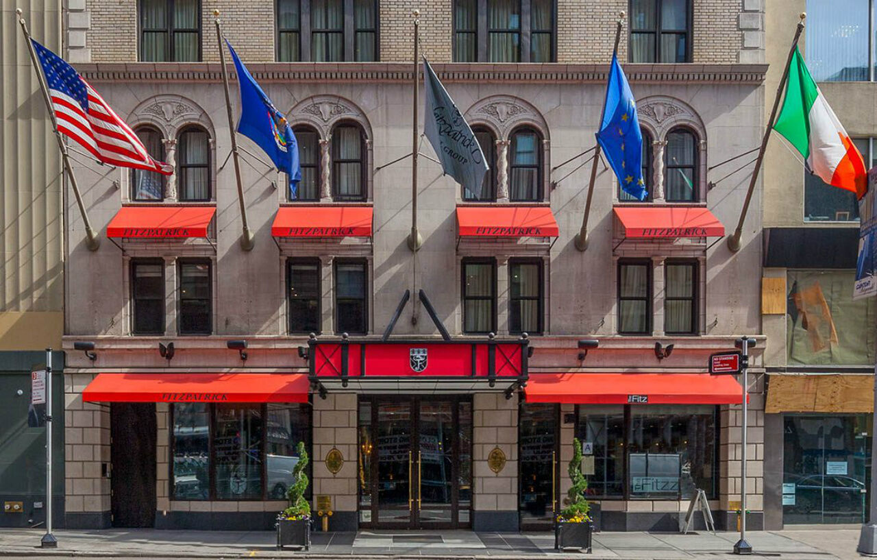 The Fitzpatrick Hotel entrance on a Manhattan street, with red awnings and a row of flags